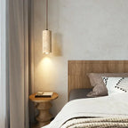 Marble cylinder pendant light hanging beside a bed with a wood headboard