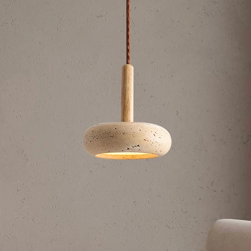 Stone disc pendant light on a wood stem hanging against a plaster wall