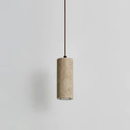 Slim marble cylinder pendant light hanging against a pale wall