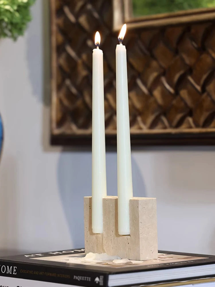 Pale taper candles in a block-shaped travertine candle holder on a dark book