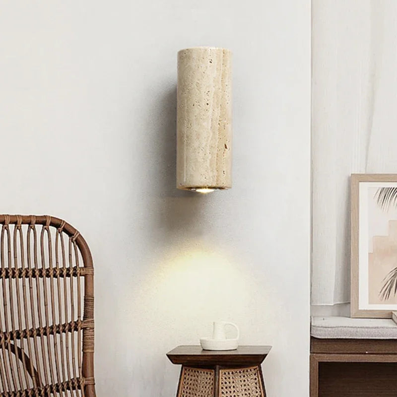 Round stone wall sconce beside a rattan chair and bedside table