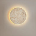 Round cave-stone wall light glowing with a warm halo on a grey wall