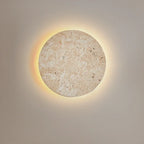 Round cave-stone wall light glowing with a warm halo on a grey wall