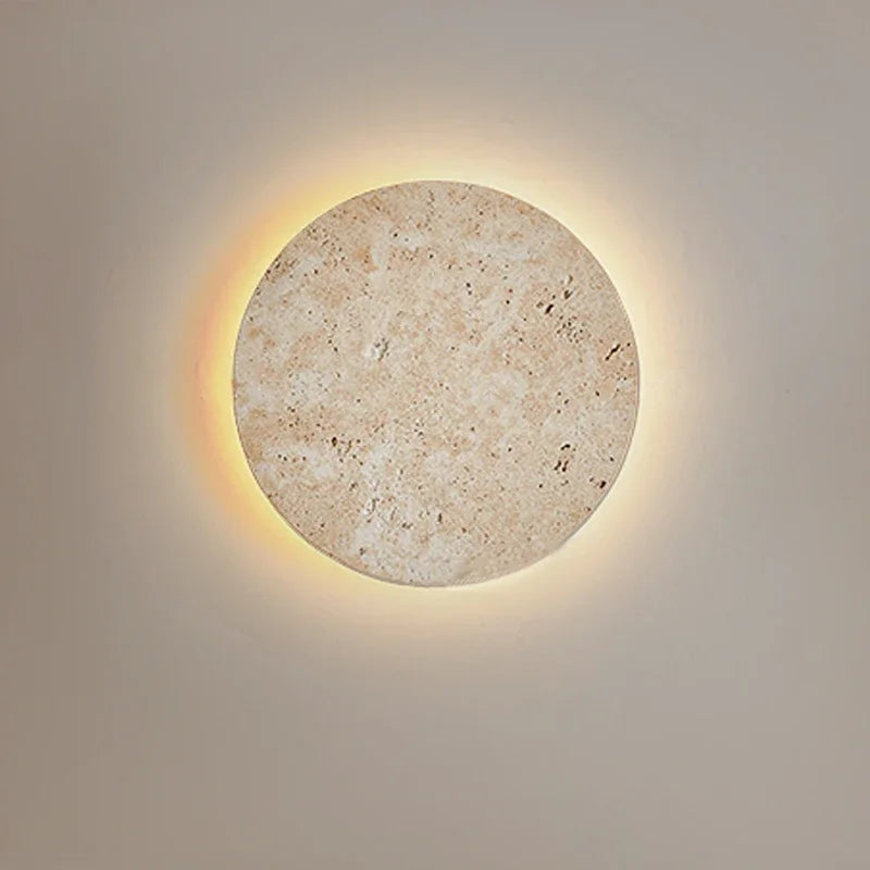 Round cave-stone wall light glowing with a warm halo on a grey wall