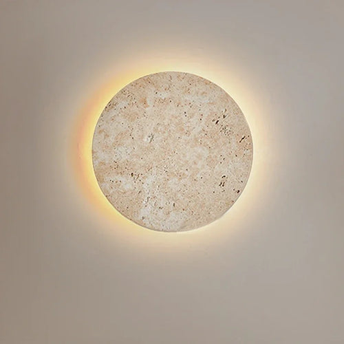 Round cave-stone wall light glowing with a warm halo on a grey wall