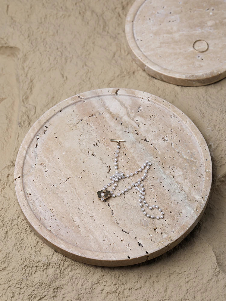 Round beige travertine tray holding a necklace on a stone surface