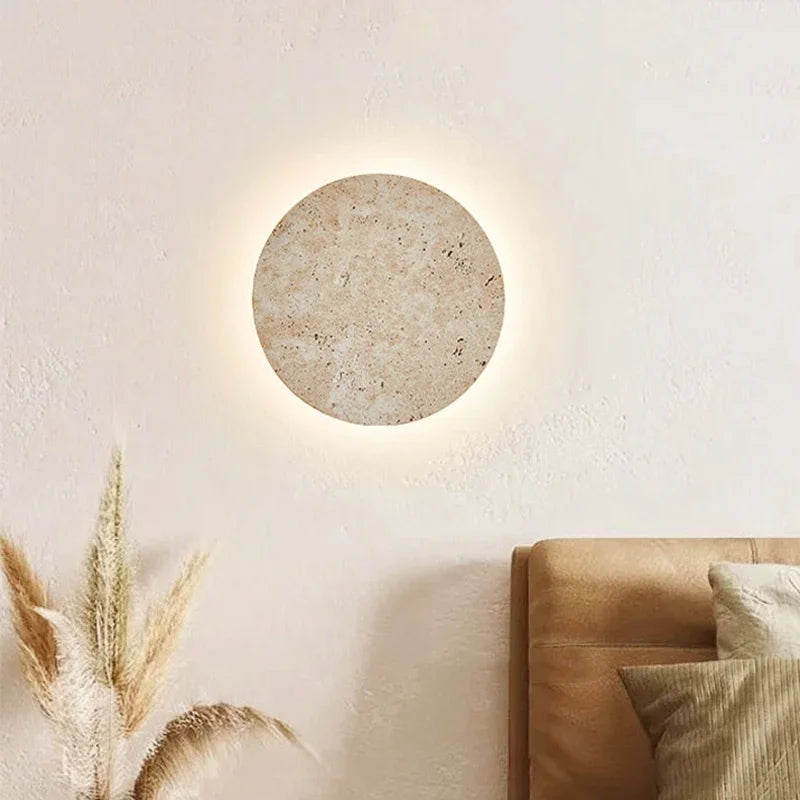 Stone disc wall light above a tan sofa with dried grasses